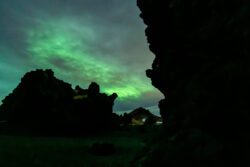 Green aurora fighting clouds among beach side rock formations dsc 4584